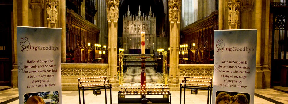 Two Saying Goodbye banners either side of rows of lit tealight candles in front of a cathedral choir screen