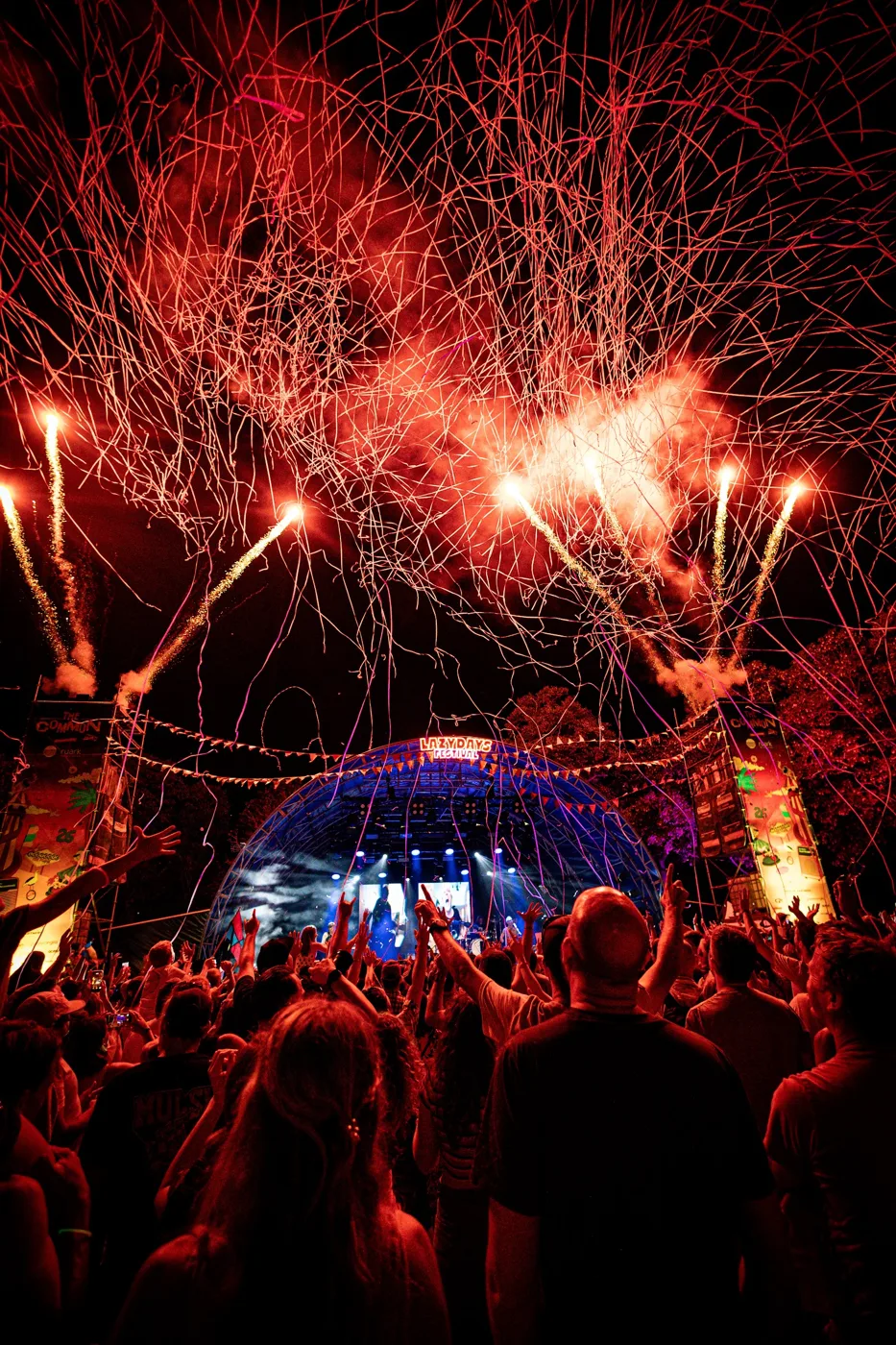 Red fireworks bursting over the main stage and a crowd at night