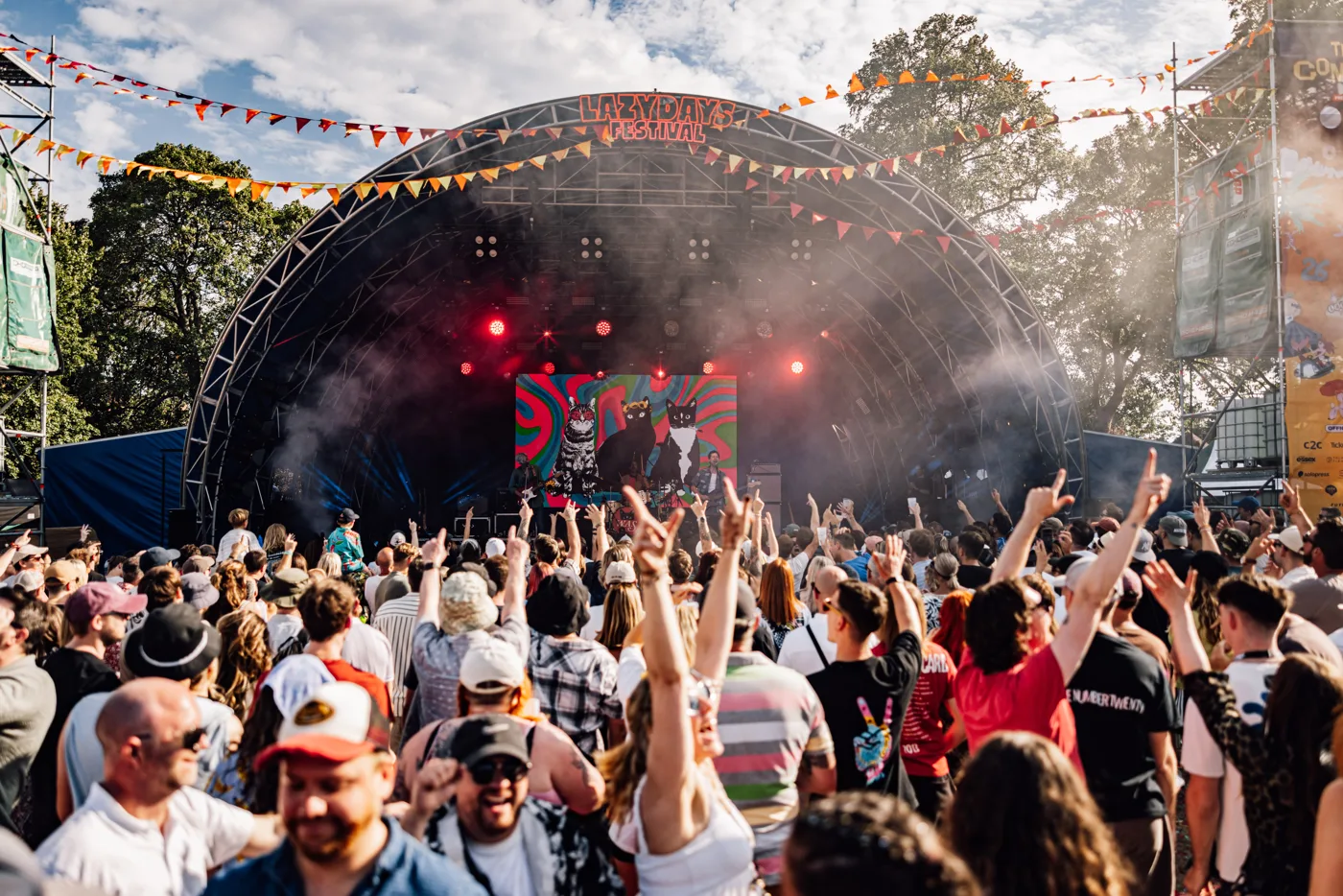 A crowd with hands raised in front of the main stage on a sunny afternoon