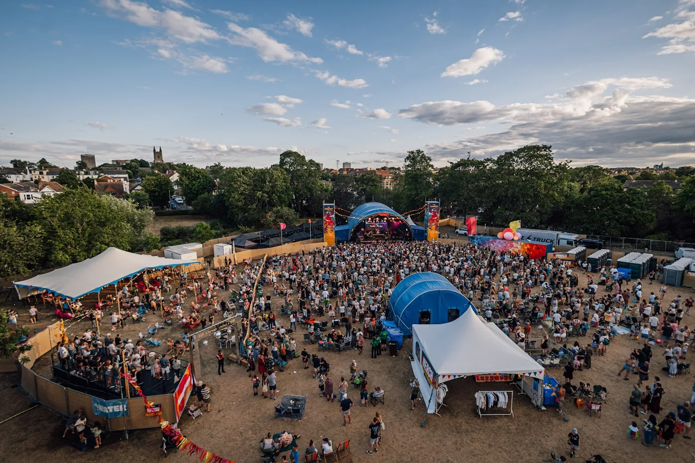 High view over the festival arena in Priory Park, with tents, a stage and the crowd on dry grass