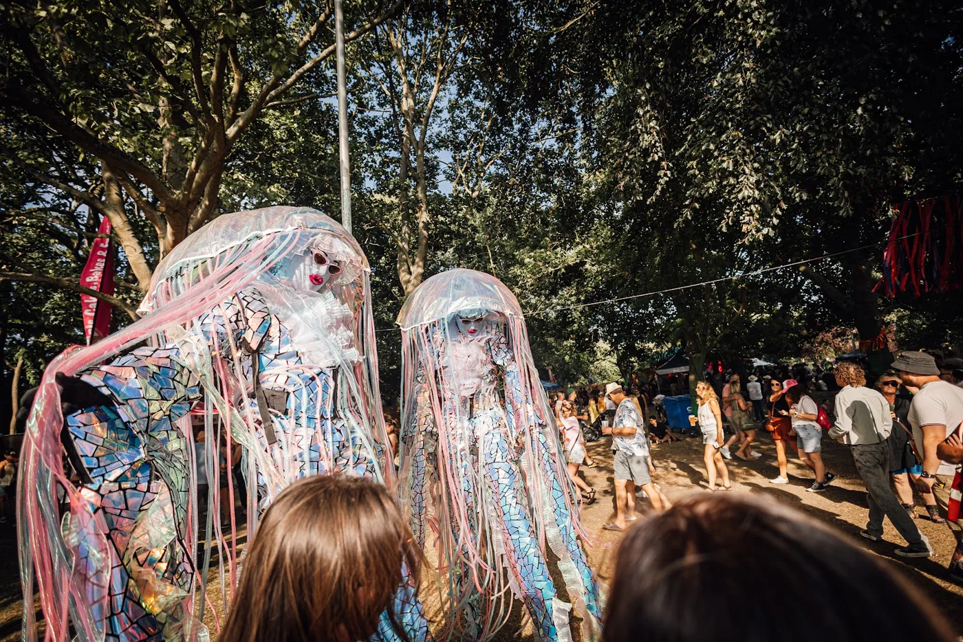 Two performers in tall jellyfish costumes made of ribbons walking through the crowd