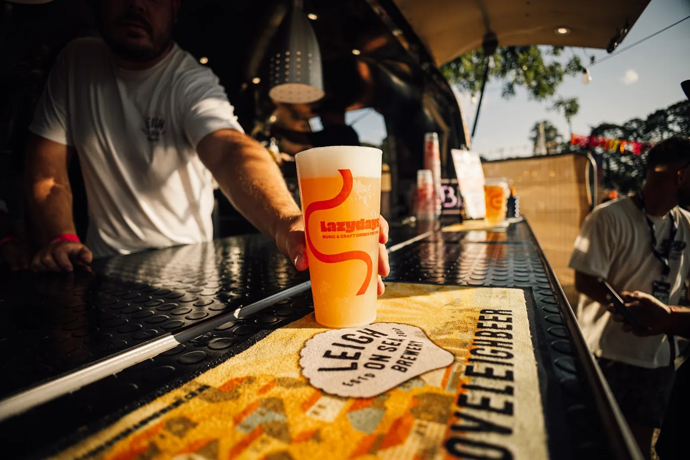 A bartender's hand setting down a Lazydays-branded cup of beer on a bar