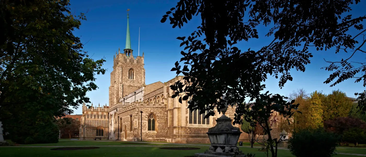 Chelmsford Cathedral's flint tower and green spire seen across the cathedral churchyard under a blue sky